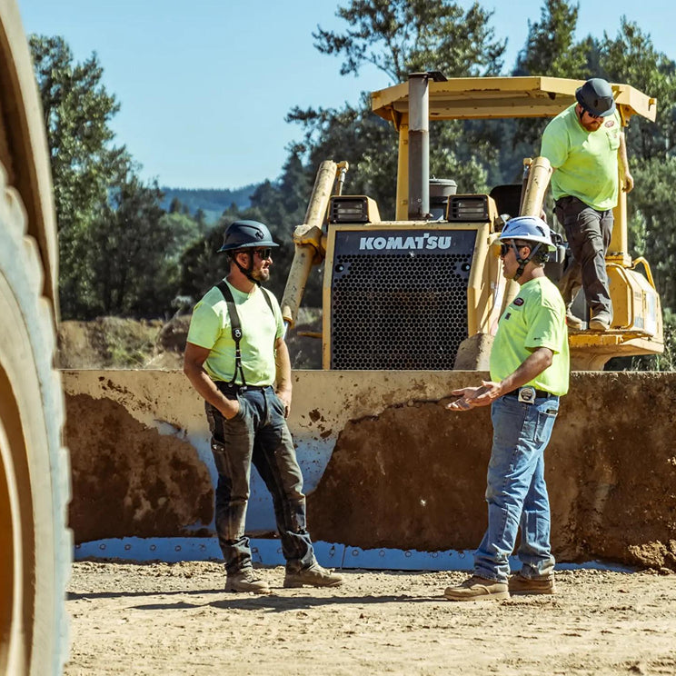 Three workers in high-visibility clothing standing next to a Komatsu bulldozer in an outdoor setting.