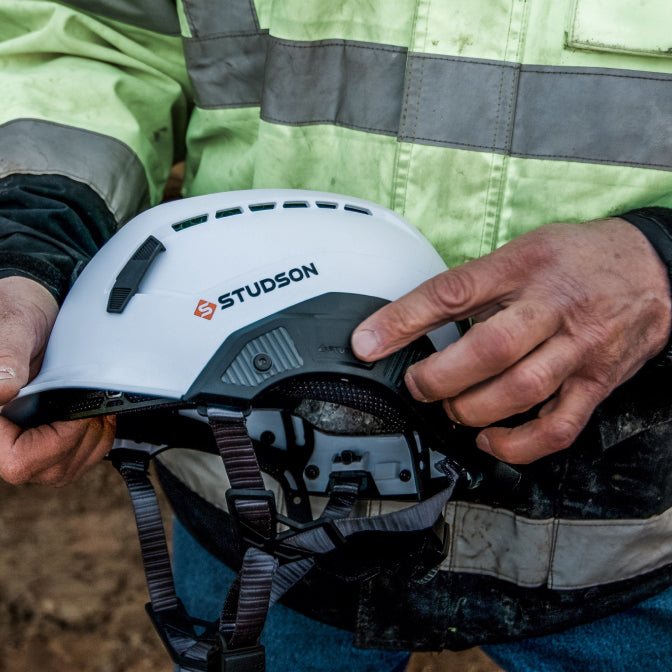 Person holding a white helmet with 'STUDSON' branding, wearing a high-visibility jacket.