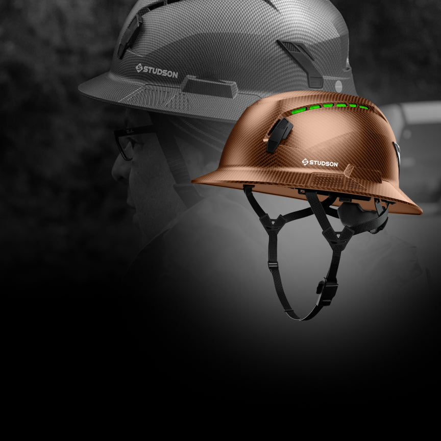 Two hard hats, one gray and one brown, with 'STUDSON' branding on a dark background.
