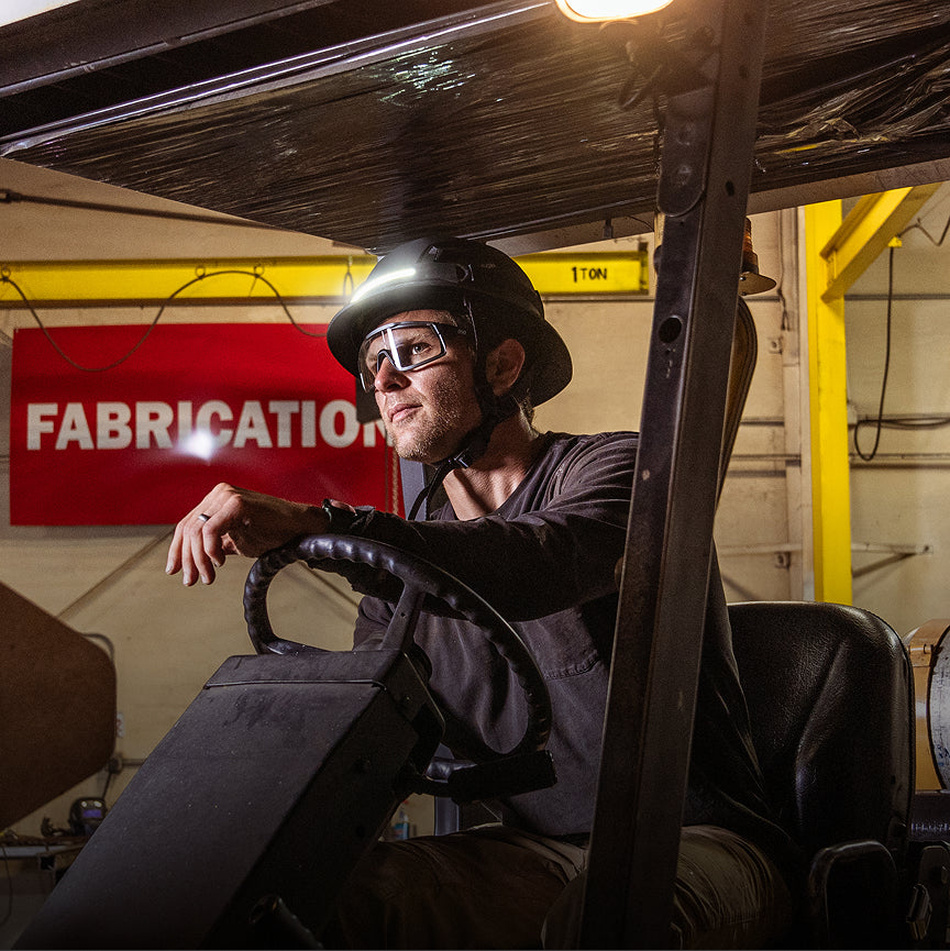 Person sitting inside a vehicle in a workshop with 'Fabrication' sign in the background