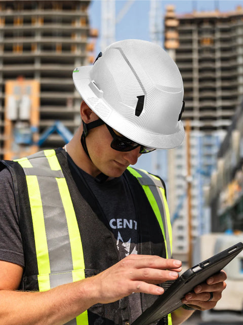 Person in construction attire using a tablet with a construction site in the background